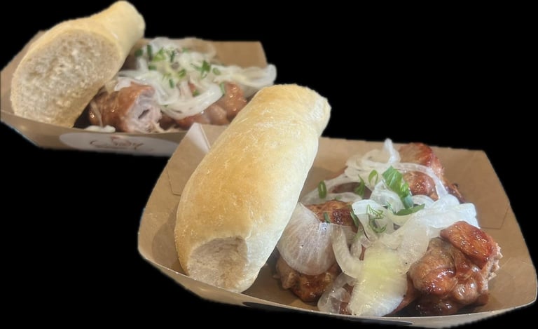 Two sandwiches on kraft paper boats with chorizo, onions, peppers, and white sauce on crusty bread rolls against a black background