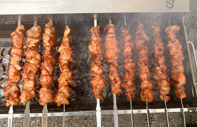 Multiple meat skewers grilling on a black griddle over charcoal, showing various stages of cooking and char marks