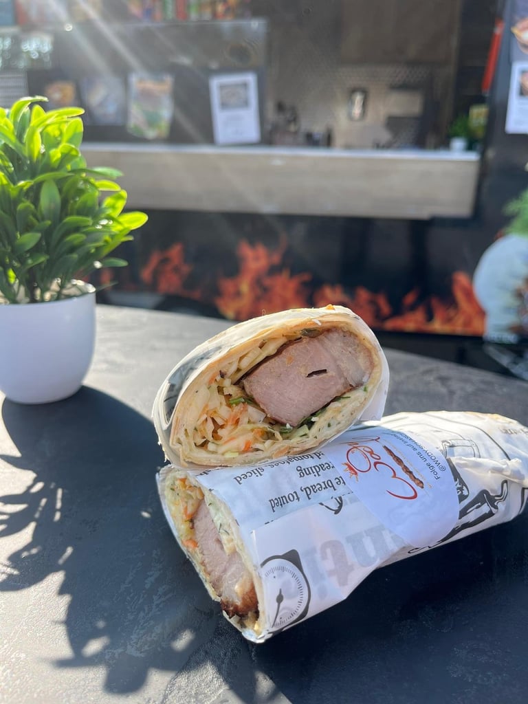 A wrapped sandwich cut in half on a dark counter with a white potted plant and restaurant interior blurred in the background