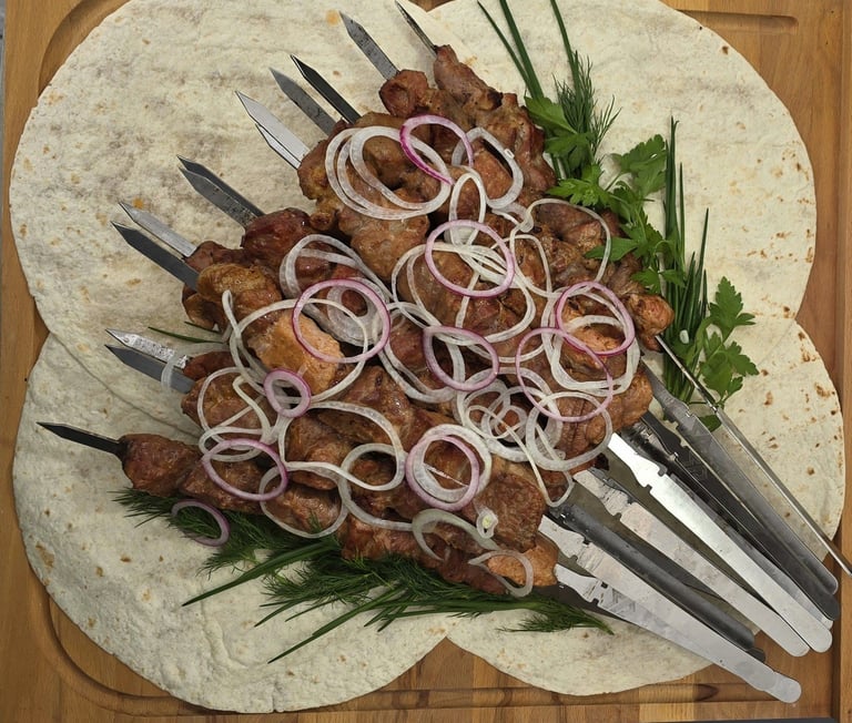 Grilled meat skewers on tortillas with sliced onions and fresh herbs on a wooden board