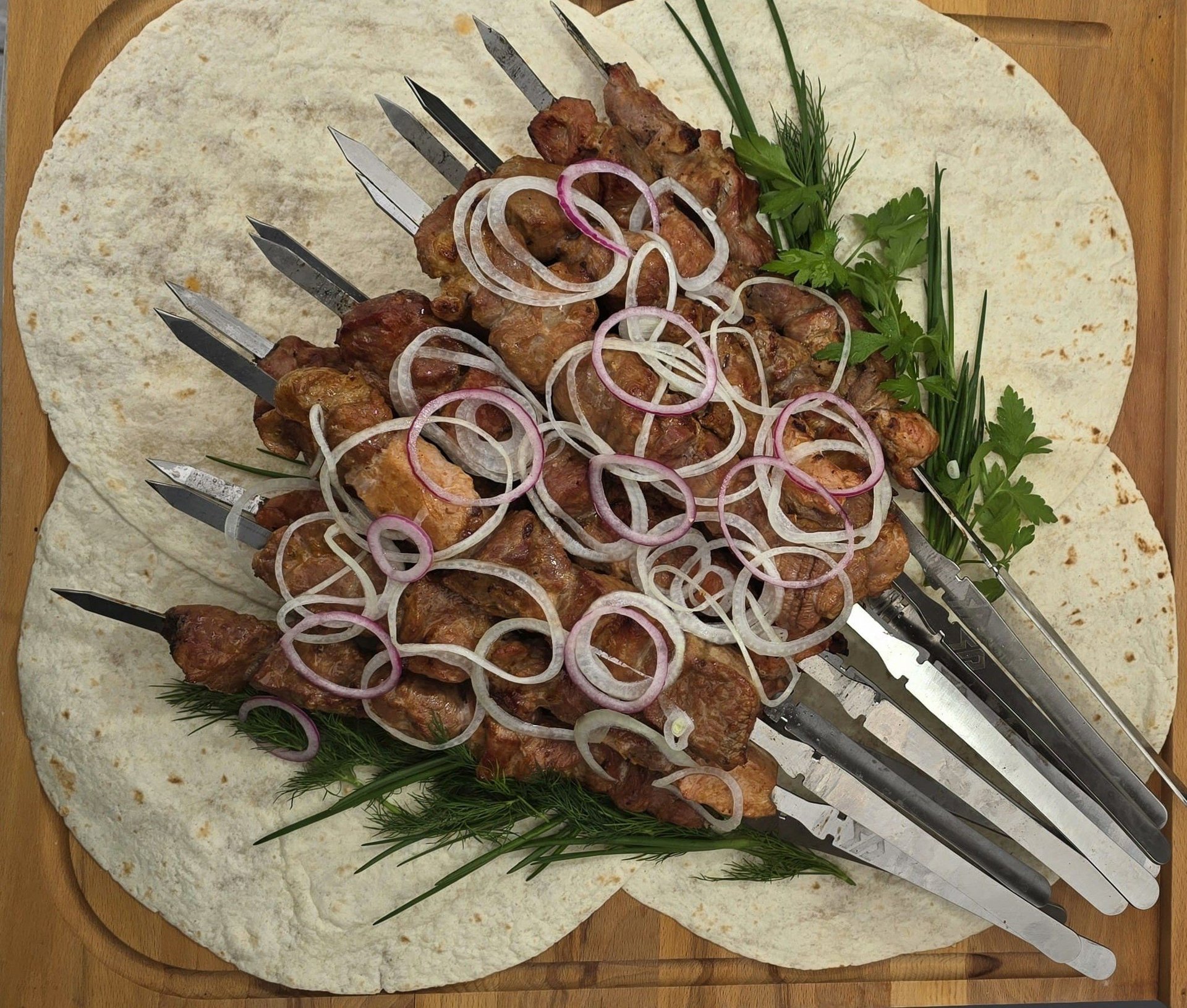 Gegrillte Schaschlik-Spieße mit Zwiebelringen und frischen Kräutern auf Fladenbrot