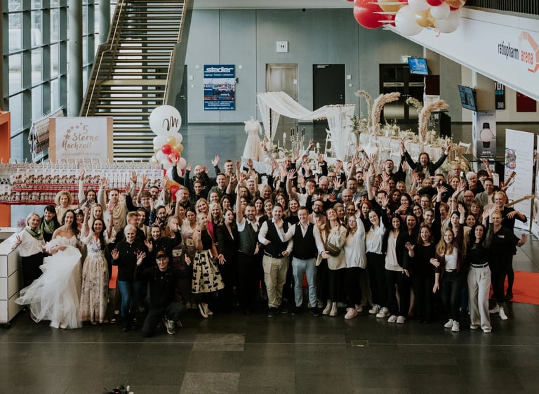 Large group of people in formal attire gathered indoors for a celebration or event, with some holding balloons and confetti