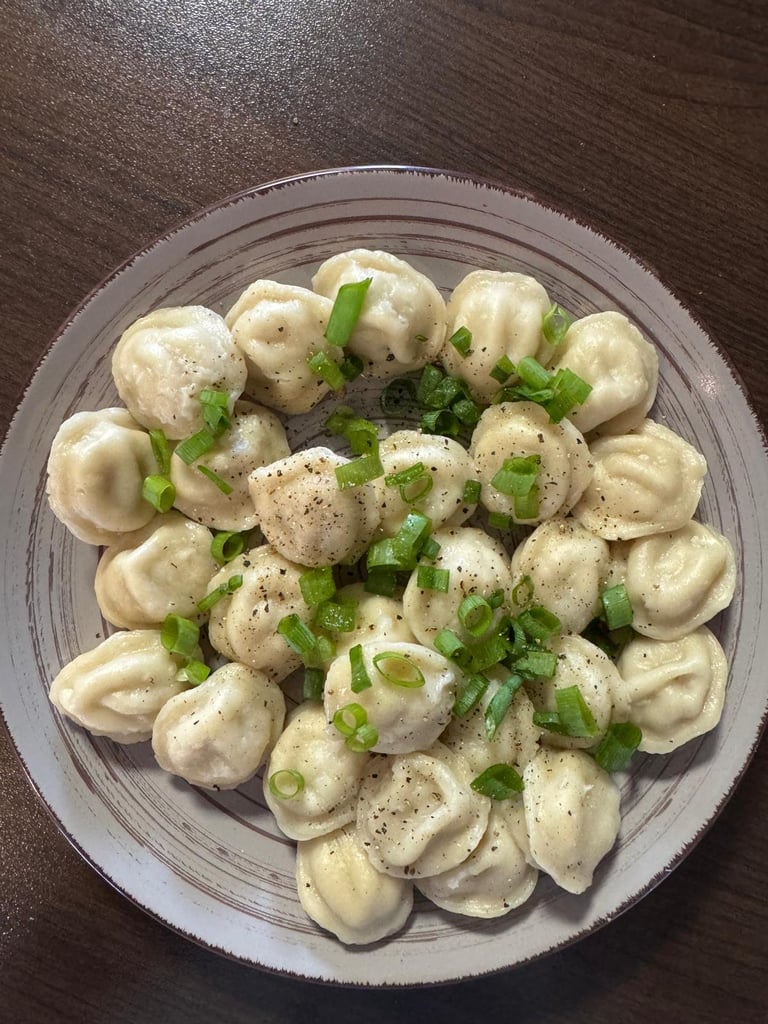 Plate of Asian dumplings topped with sliced green onions and black pepper on a gray plate
