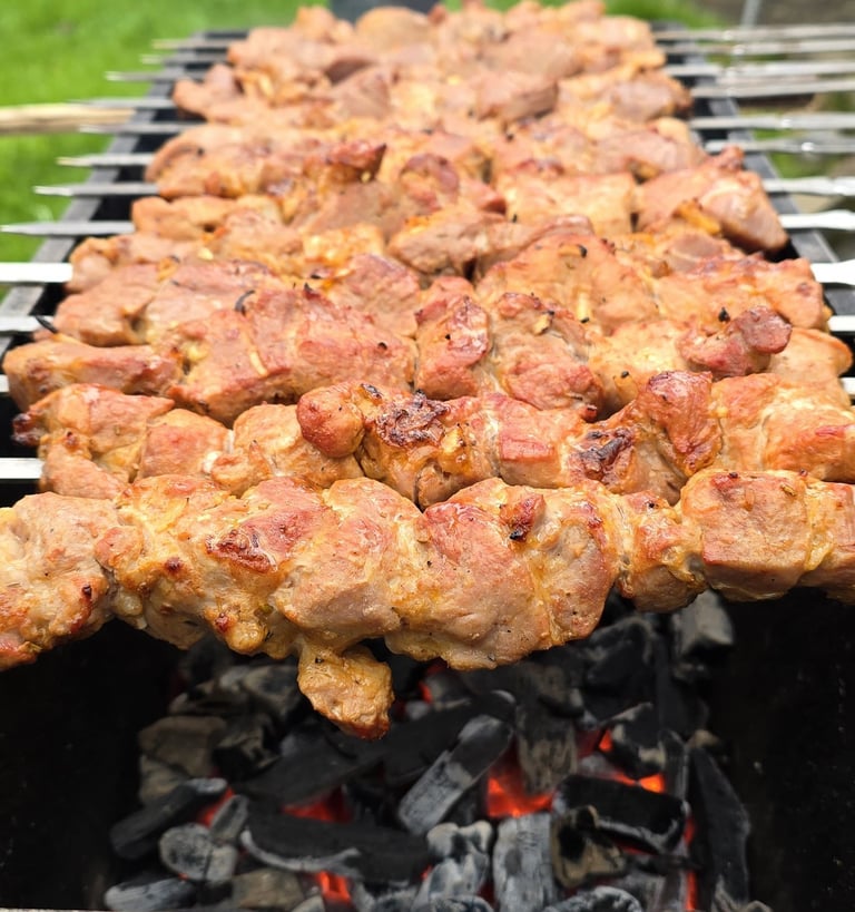 Meat skewers grilling over charcoal flame with green grass visible in background